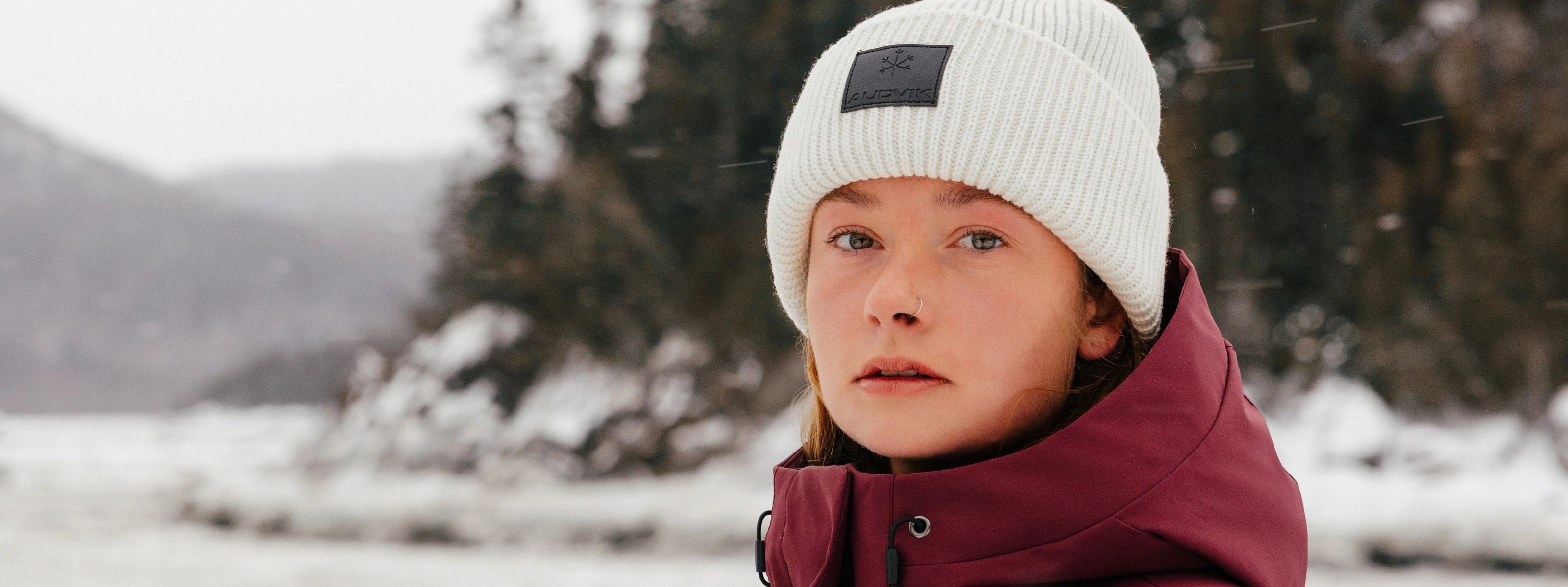 Femme portant une tuque beige Audvik dans un paysage hivernal.